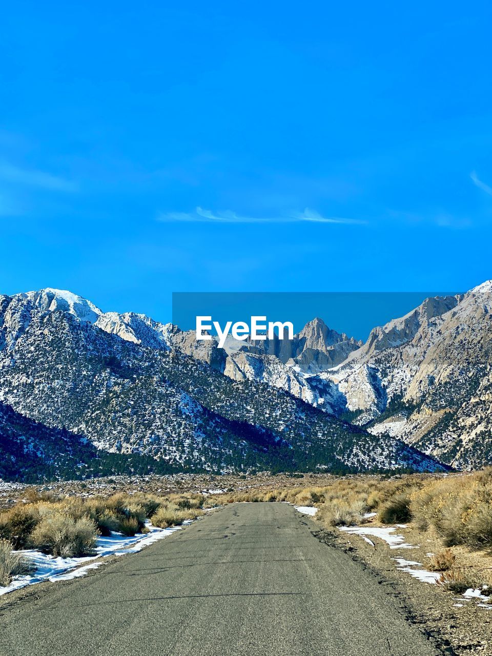 Road amidst snowcapped mountains against blue sky