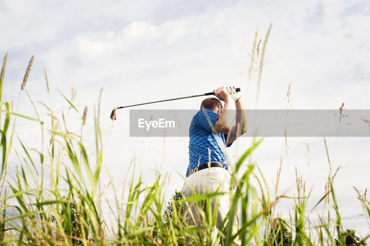 Rear view of man playing golf on field against sky