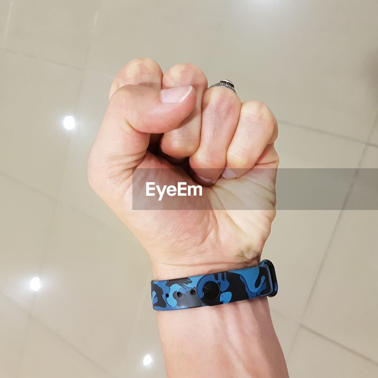 Close-up of man wearing blue wristwatch clenching fist over tiled floor