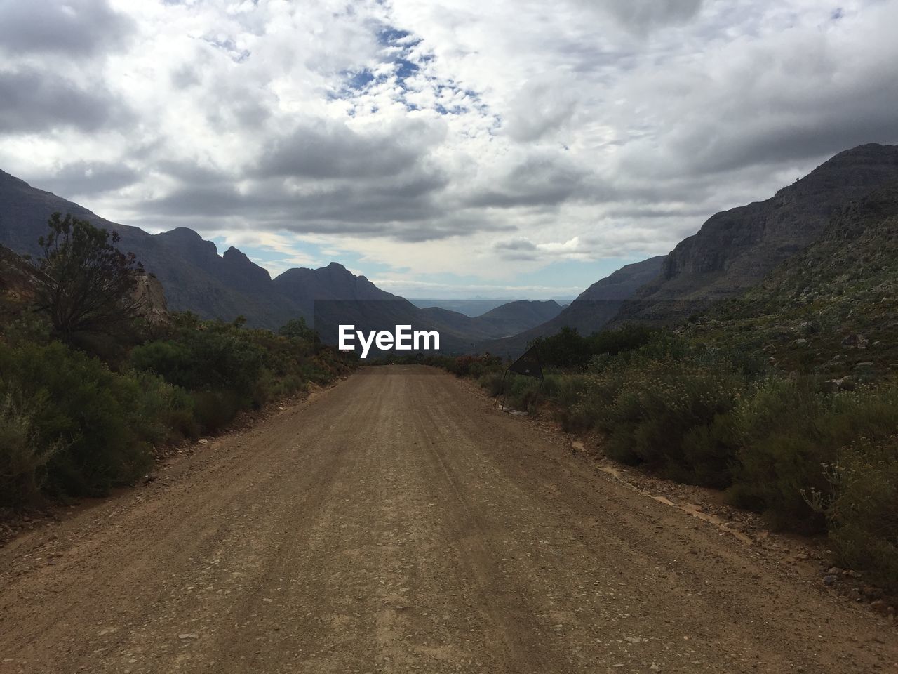 Dirt road against cloudy sky