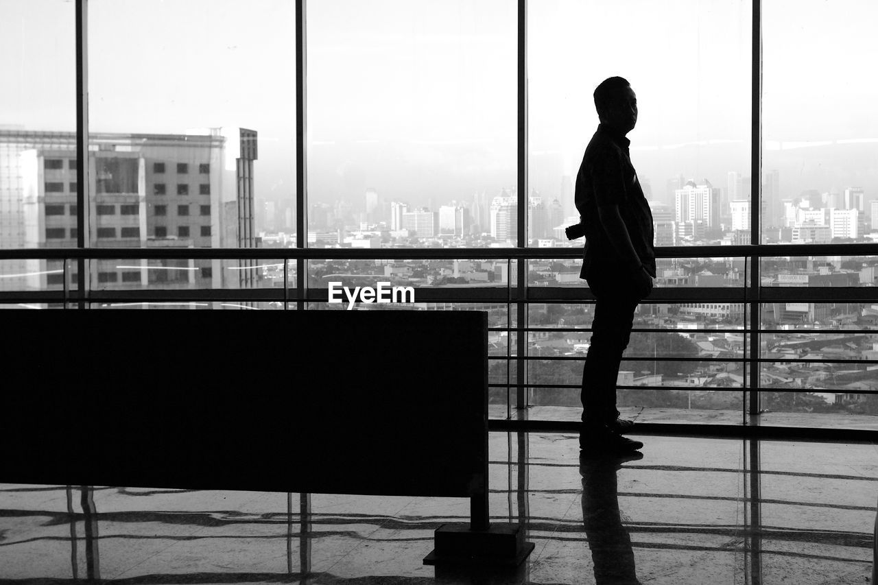 Silhouette man standing by window against city