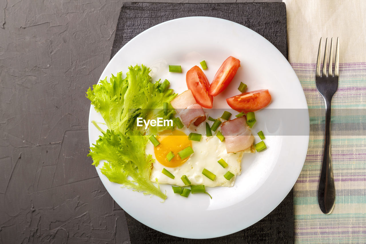 Scrambled eggs with bacon garnished with tomato and green onions and salad on a gray concrete