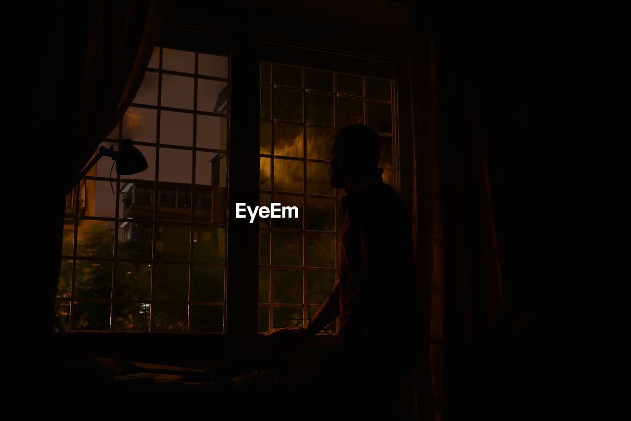 Man standing by window at dusk