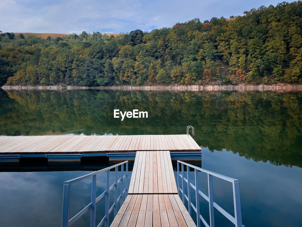 Wooden pontoon on a lake surrounded by forest beginning to change colors in autumn