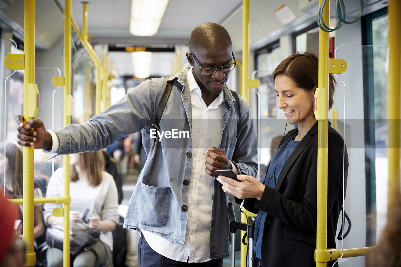 Multi-ethnic commuters sharing smart phone while standing in tram