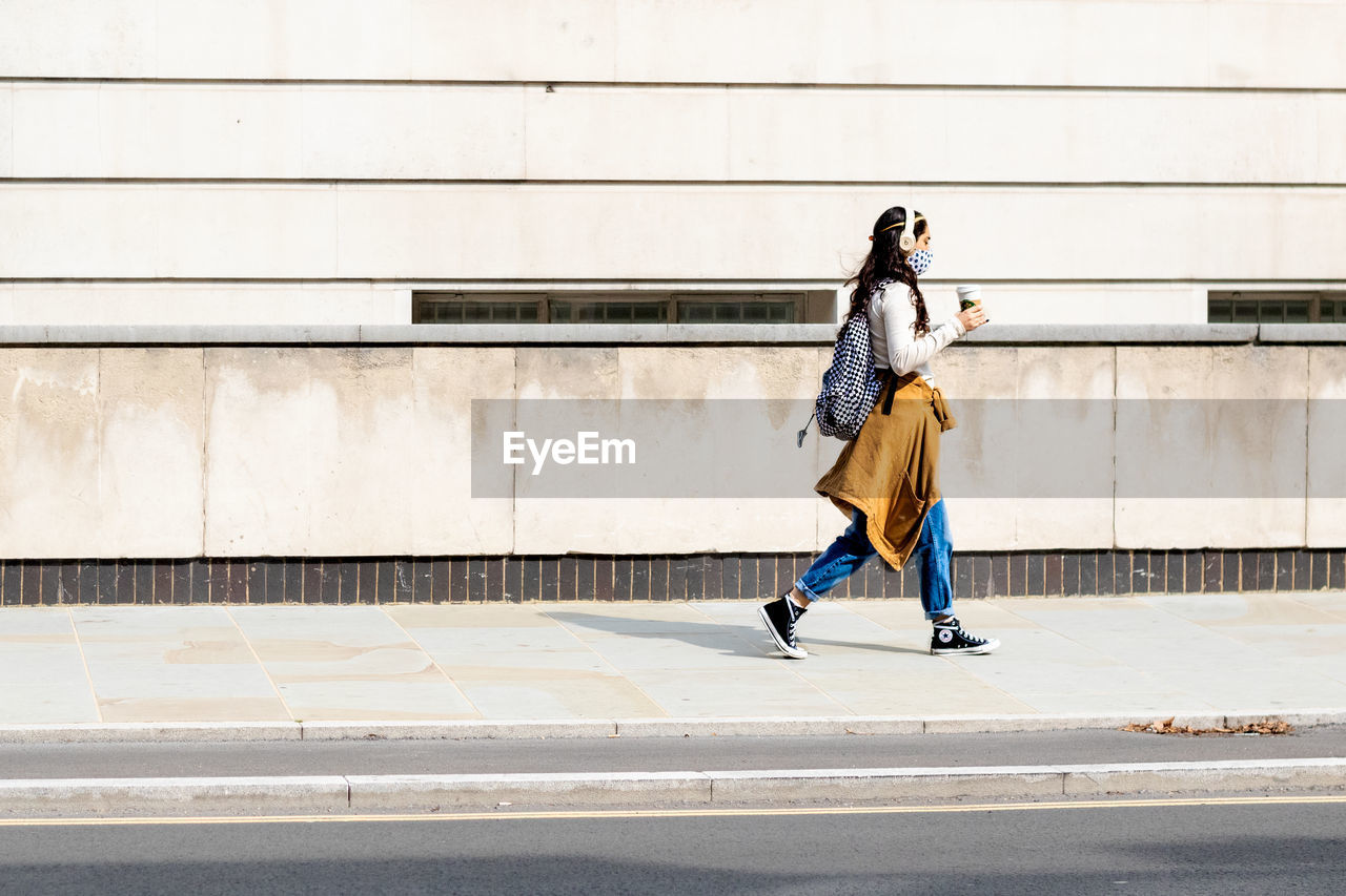 FULL LENGTH SIDE VIEW OF WOMAN WALKING ON FOOTPATH IN CITY