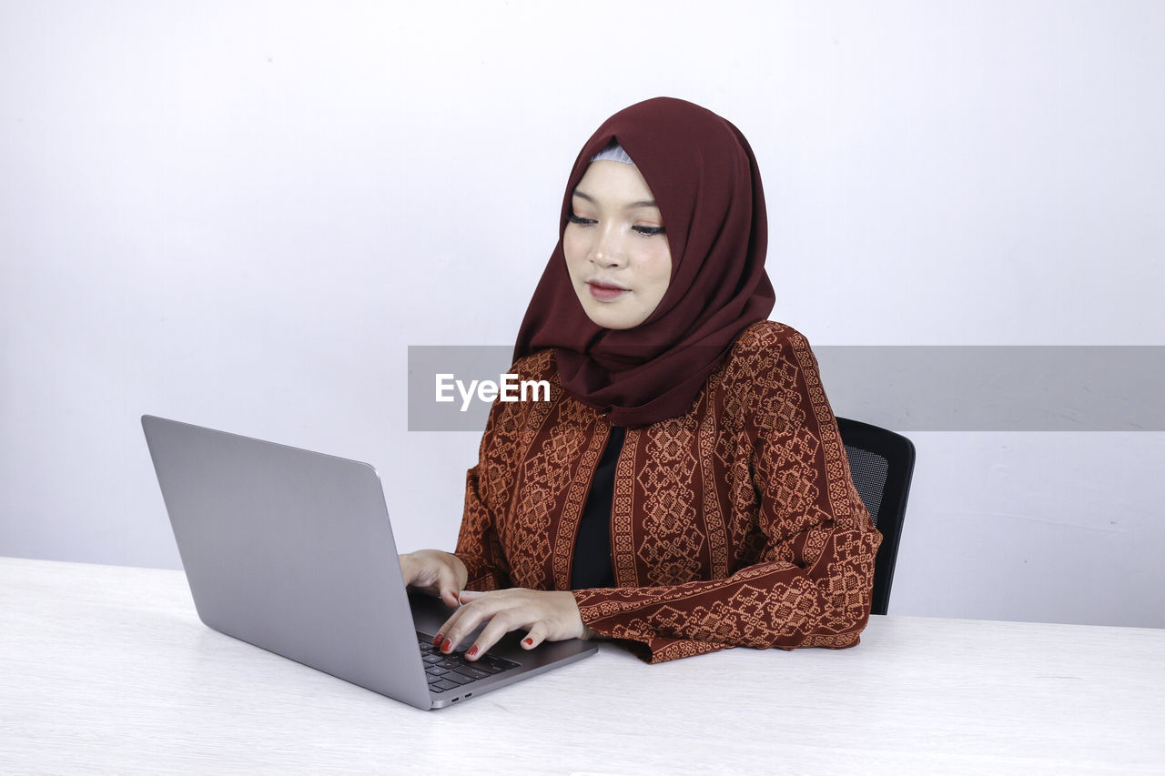 WOMAN LOOKING AT CAMERA WHILE SITTING ON LAPTOP