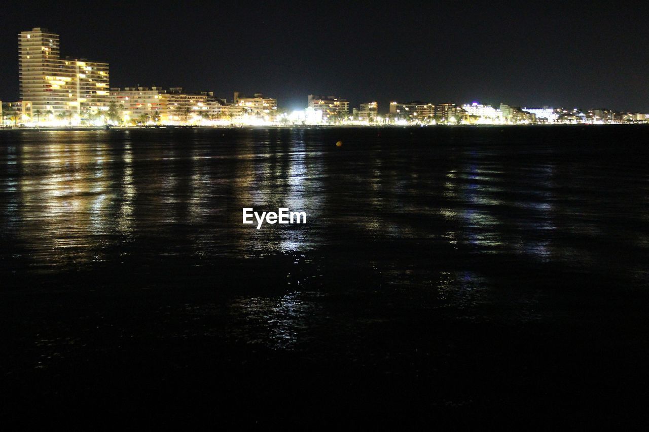 SEA BY ILLUMINATED CITY BUILDINGS AT NIGHT