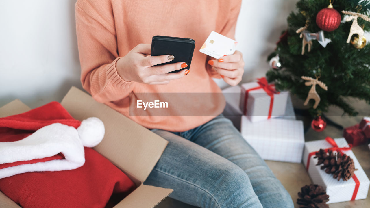 Midsection of woman holding credit card while using phone