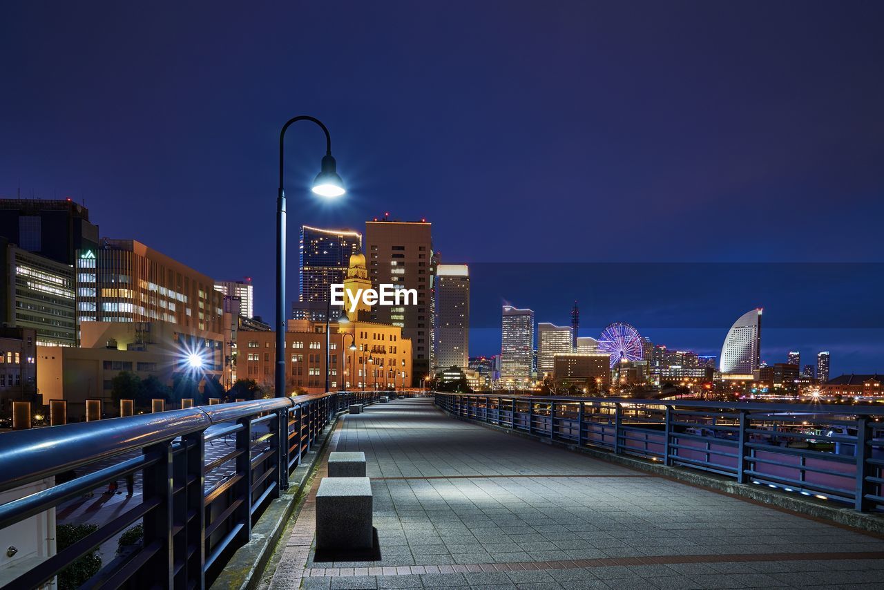 Illuminated street amidst buildings against sky at night