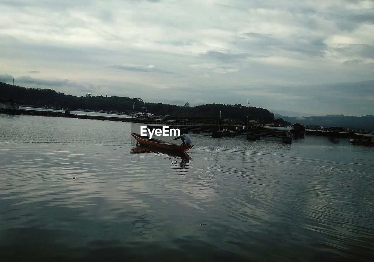 MAN ROWING BOAT ON RIVER AGAINST SKY