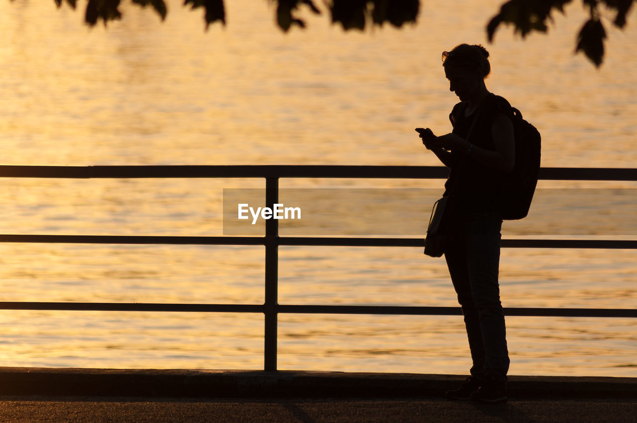 Silhouette woman using smart phone by railing against sea