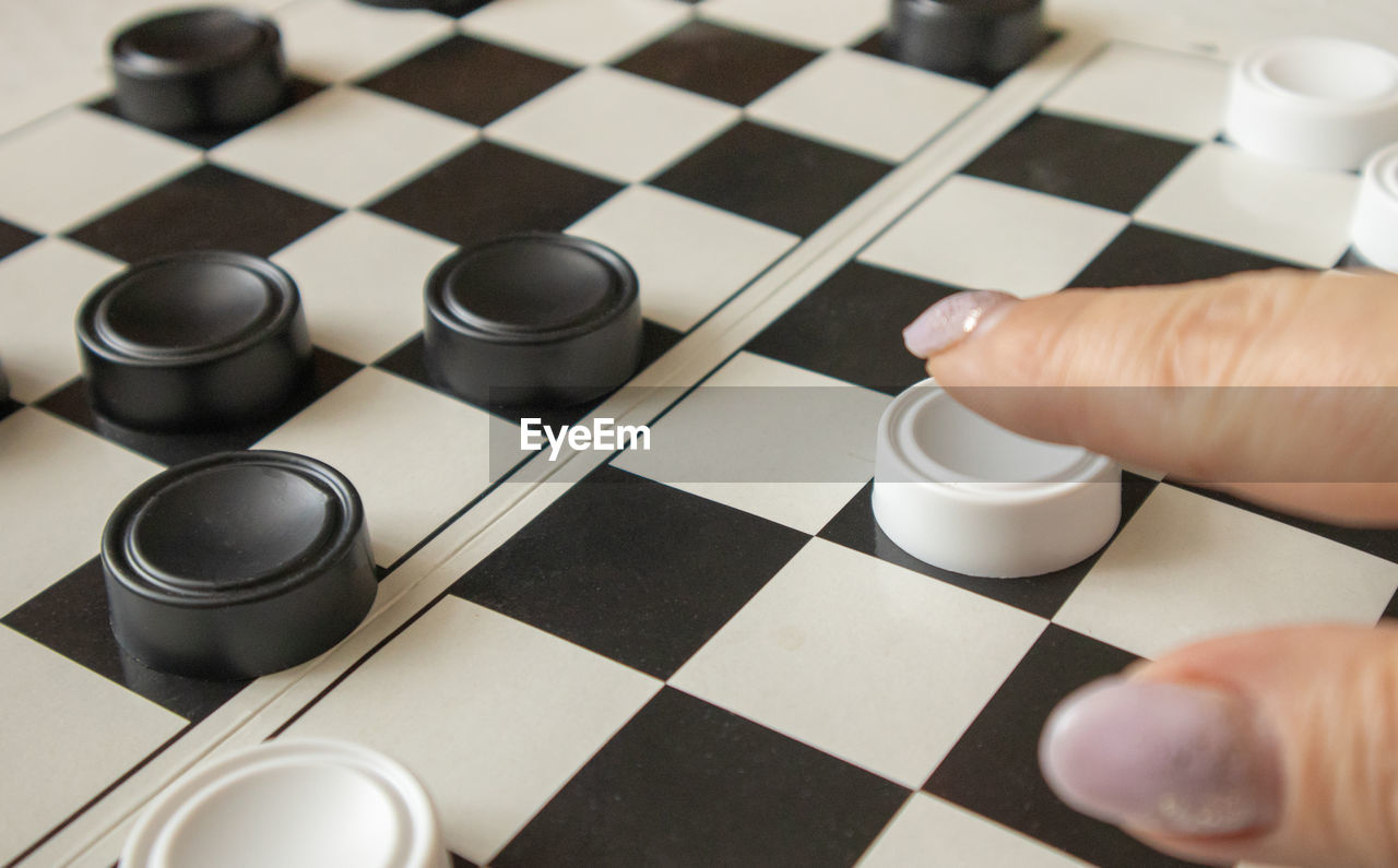 A woman's hand moves a white checker on a black-and-white playing field, the concept of hobbies 
