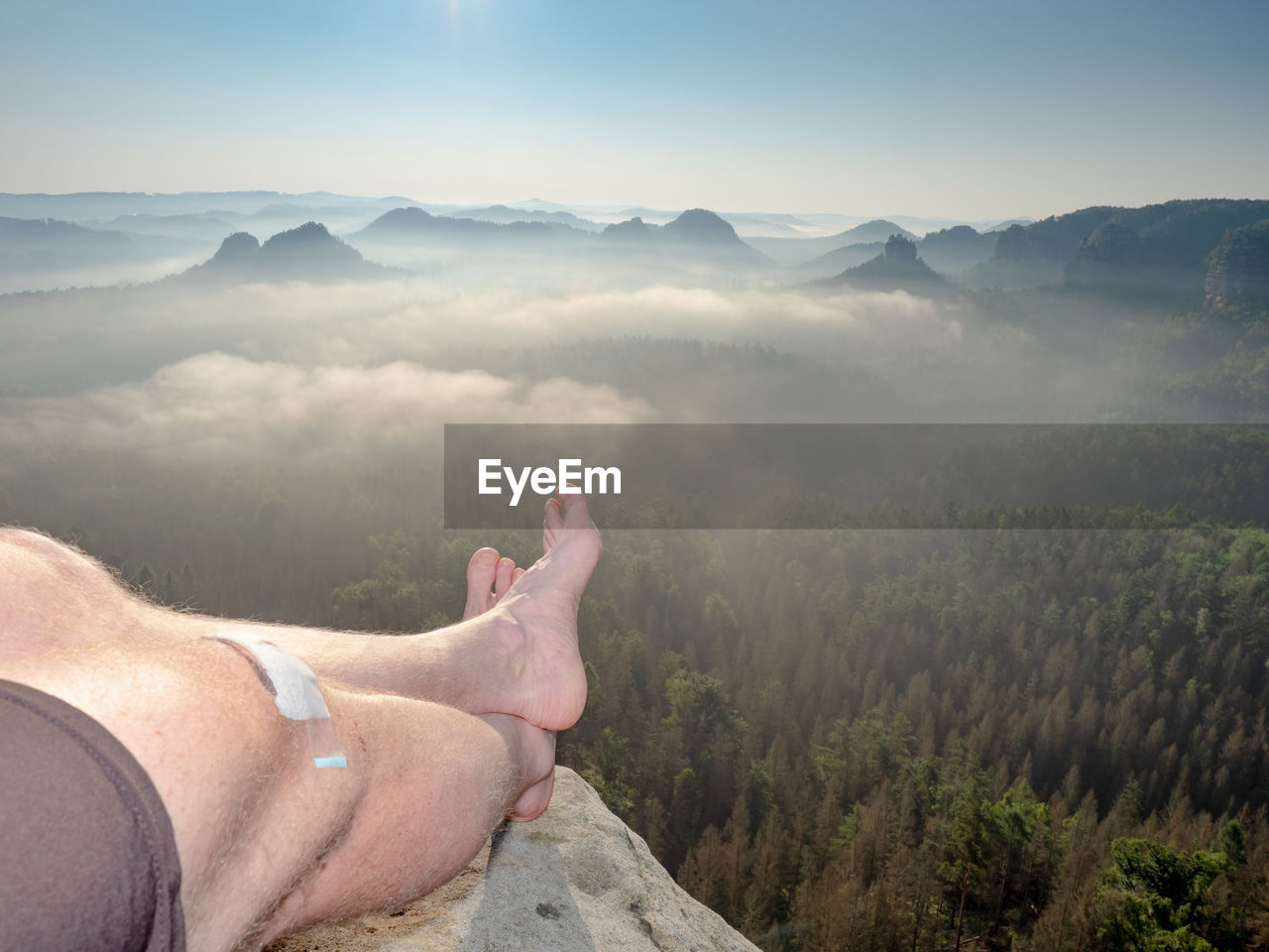 Hiker lie on edge of rock massif and relax. view over crossed legs of resting body into landscape