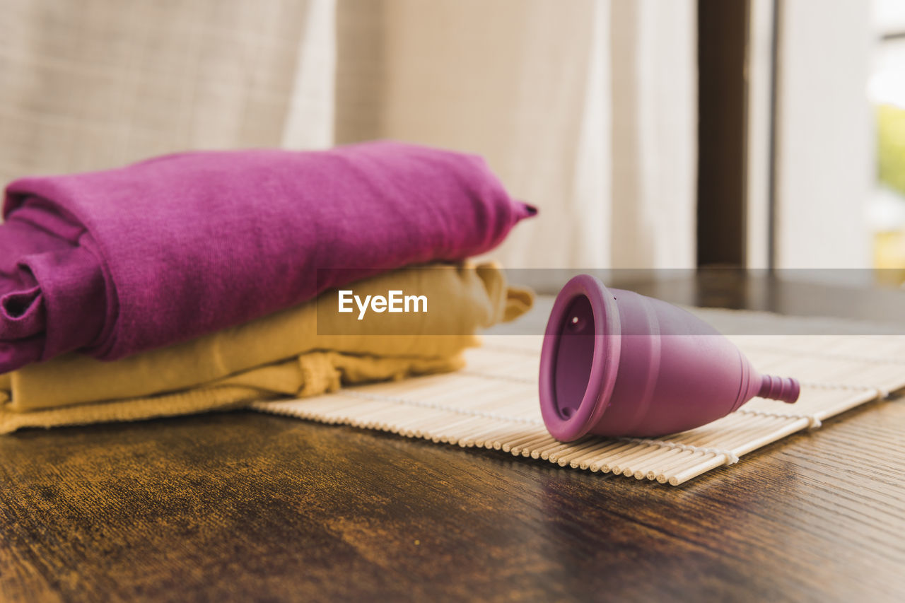 Menstrual cup on bamboo mat at table by colored clothes