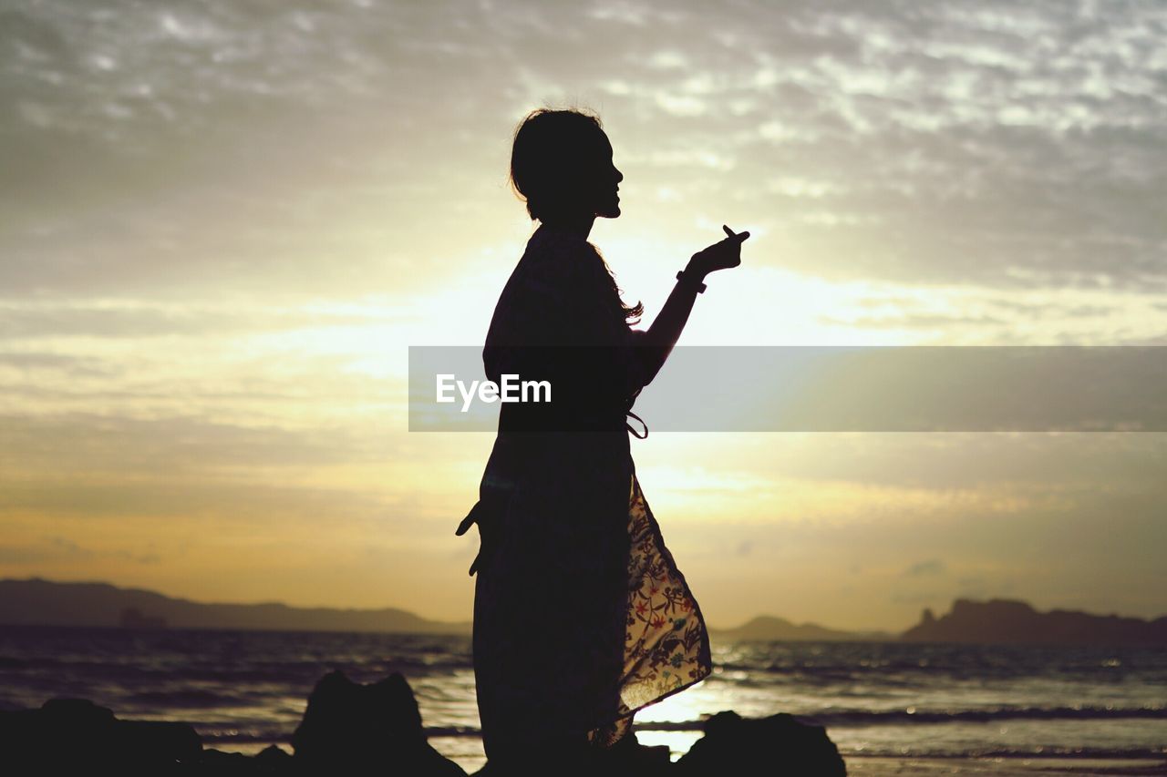 Silhouette woman standing at beach against sky during sunset