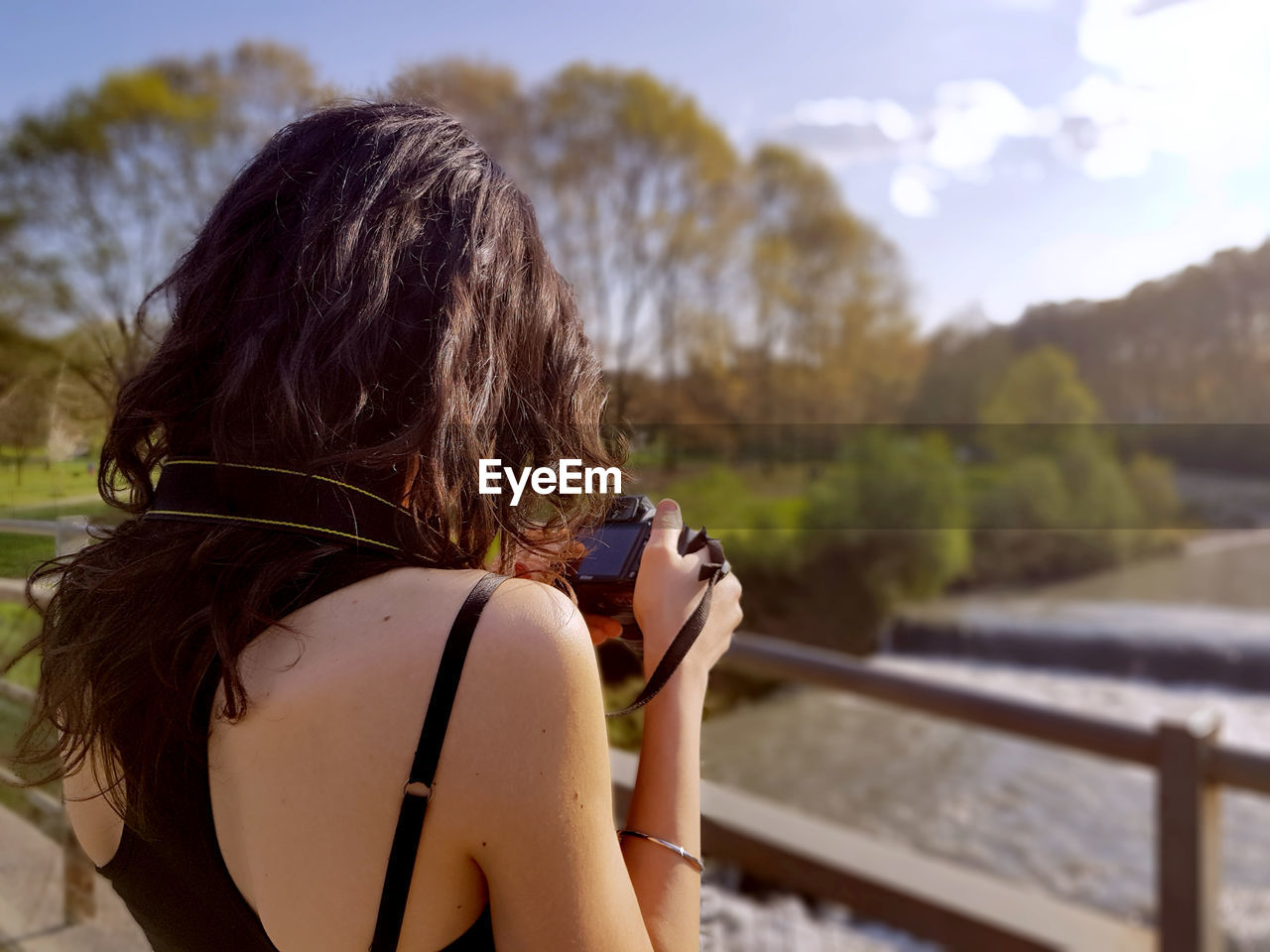 Rear view of woman with camera standing on footbridge