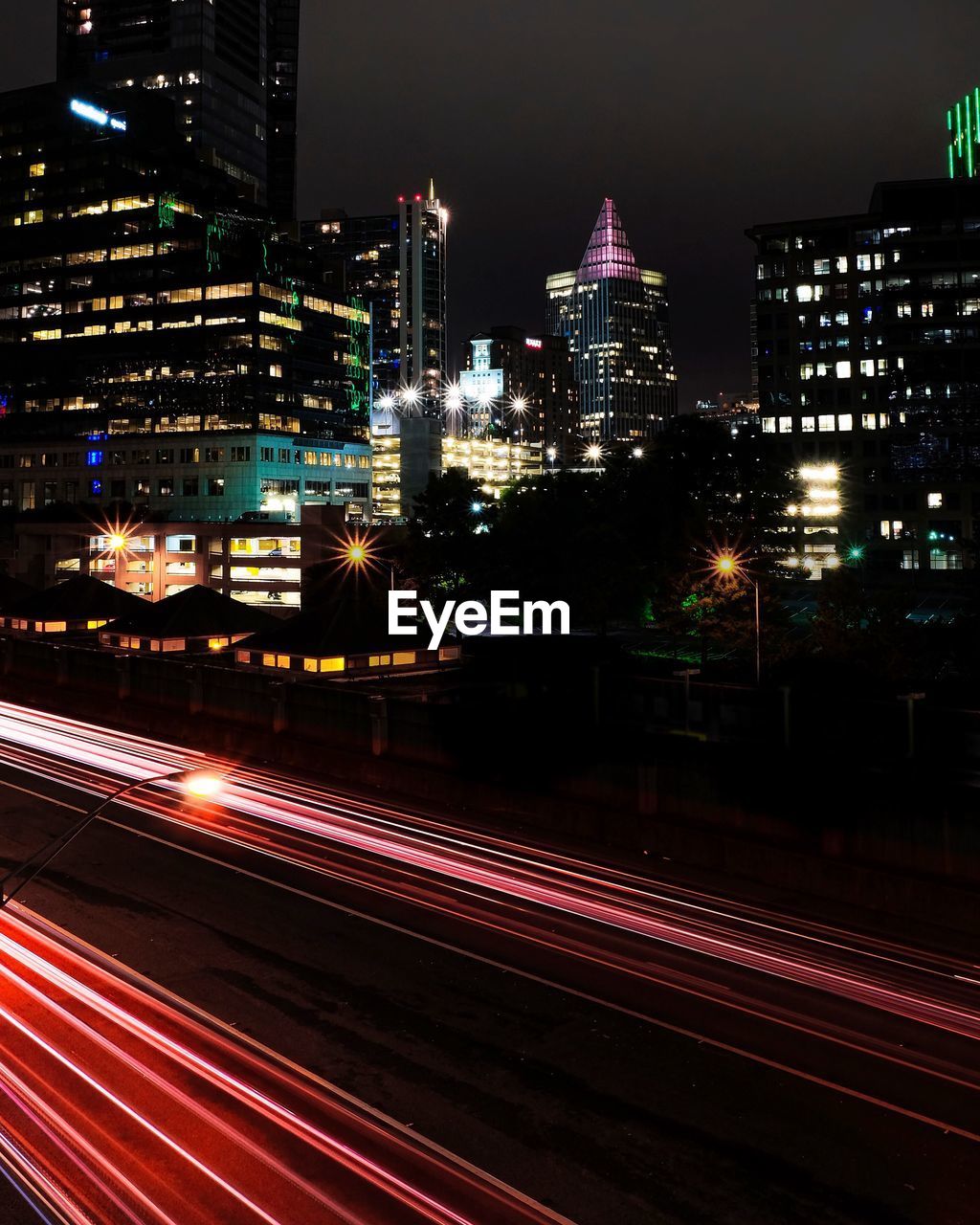 LIGHT TRAILS ON STREET AGAINST ILLUMINATED BUILDINGS IN CITY