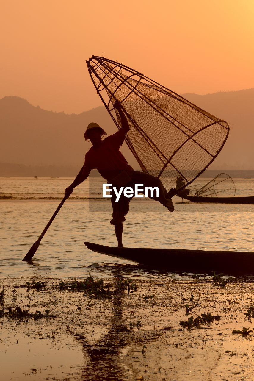 Fisherman fishing in lake with conical fishing nets during sunset