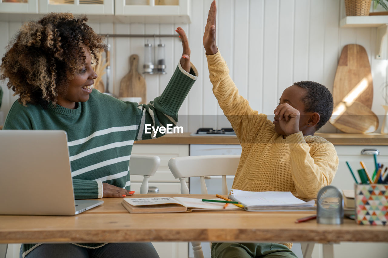 Happy african american mother and son giving each other high fives while studying together at home