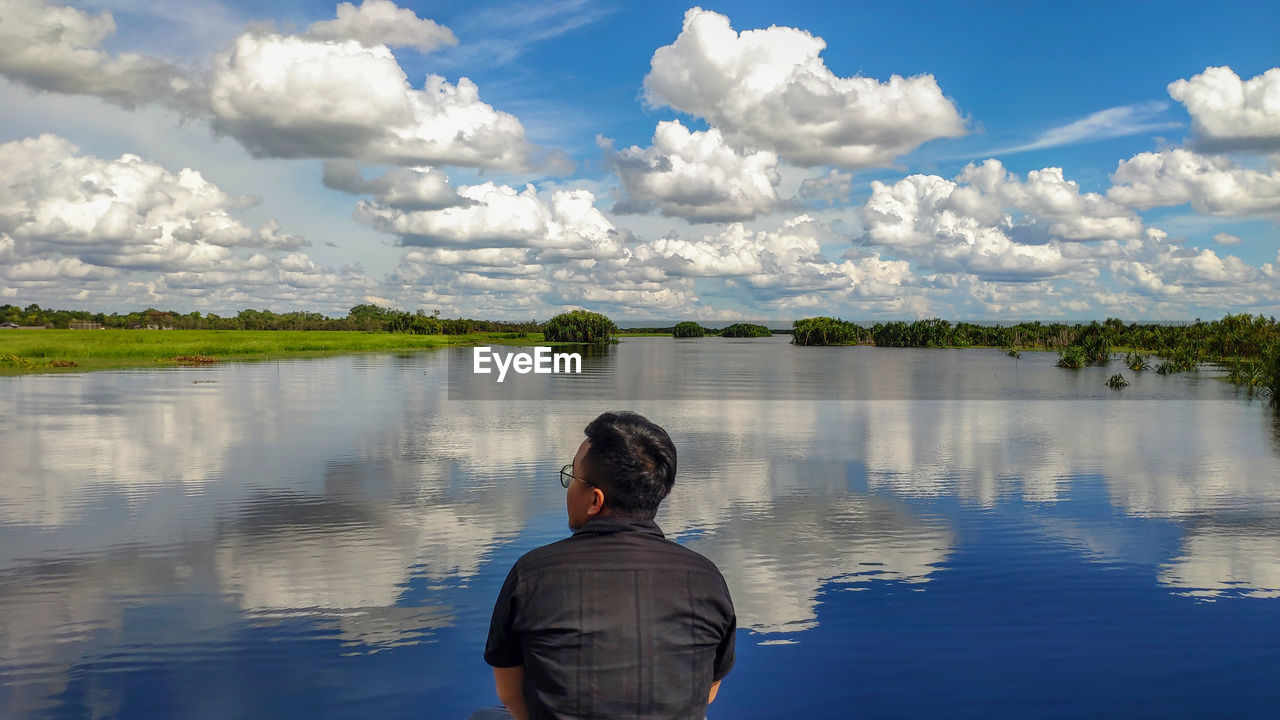 Rear view of man looking at lake against cloudy sky