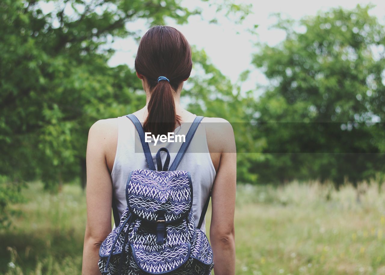 Rear view of backpack woman standing on grassy field