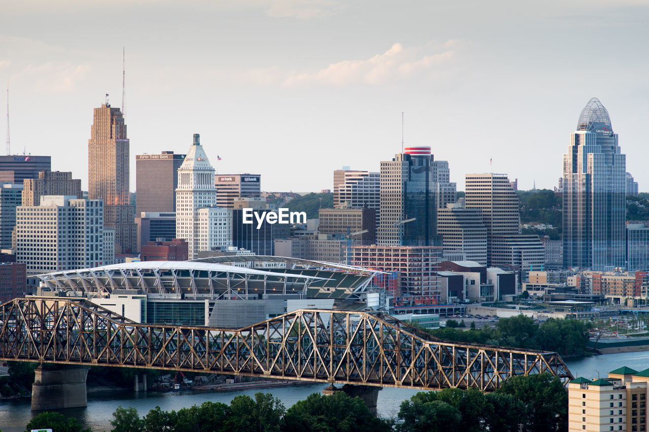 Brent spence bridge over ohio river by modern buildings against sky during sunset