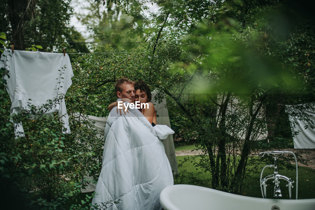 Couple with towel standing against trees