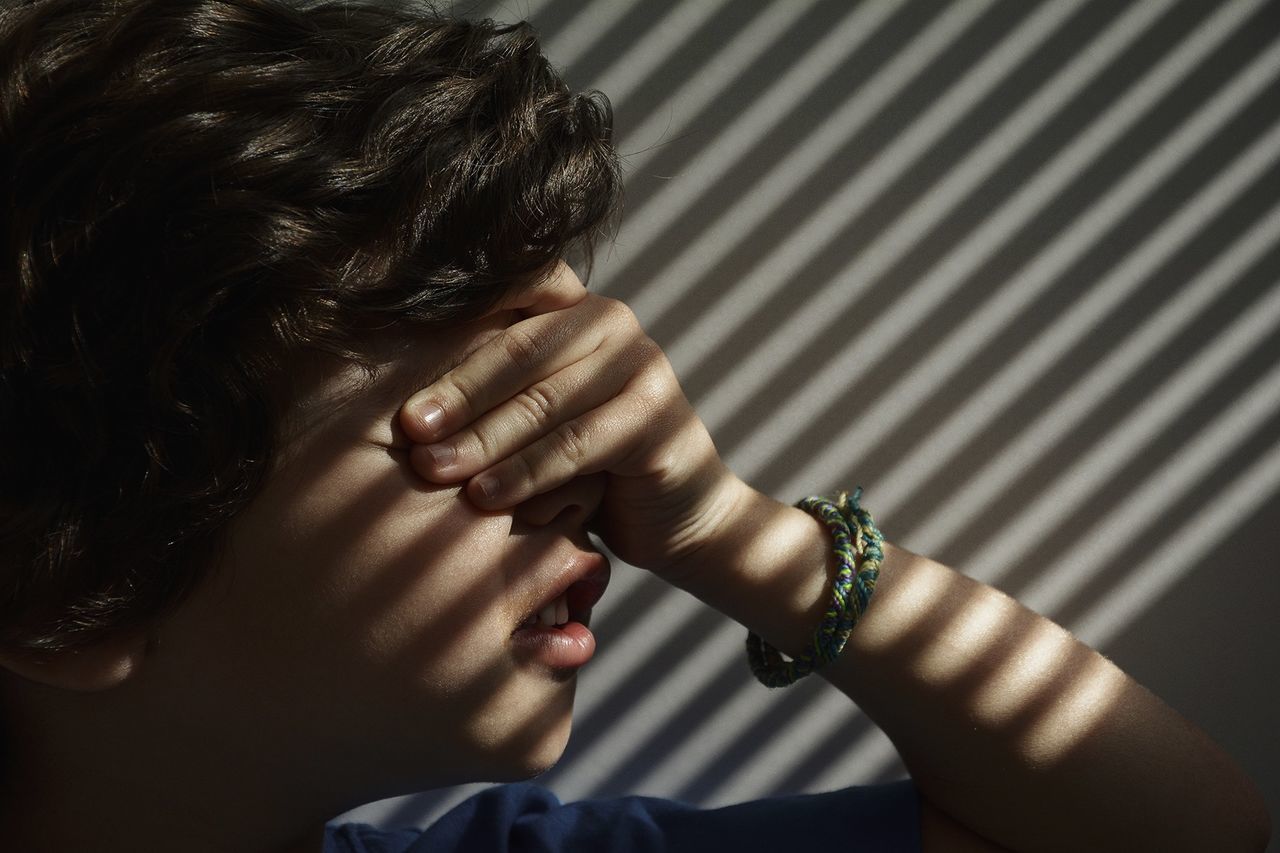 Cute boy with eyes closed against wall with shadow of blinds