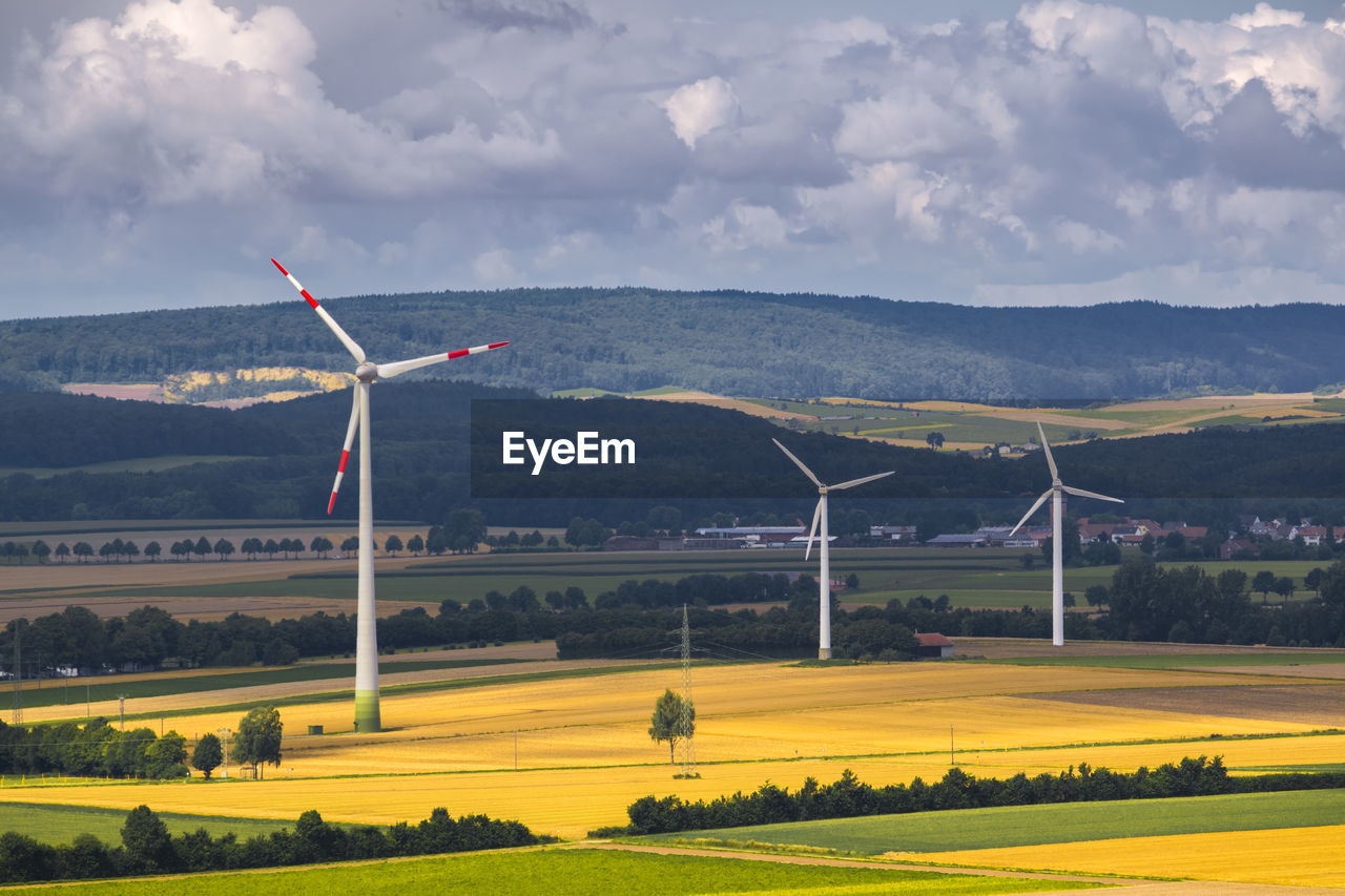 Wind turbines on field against sky