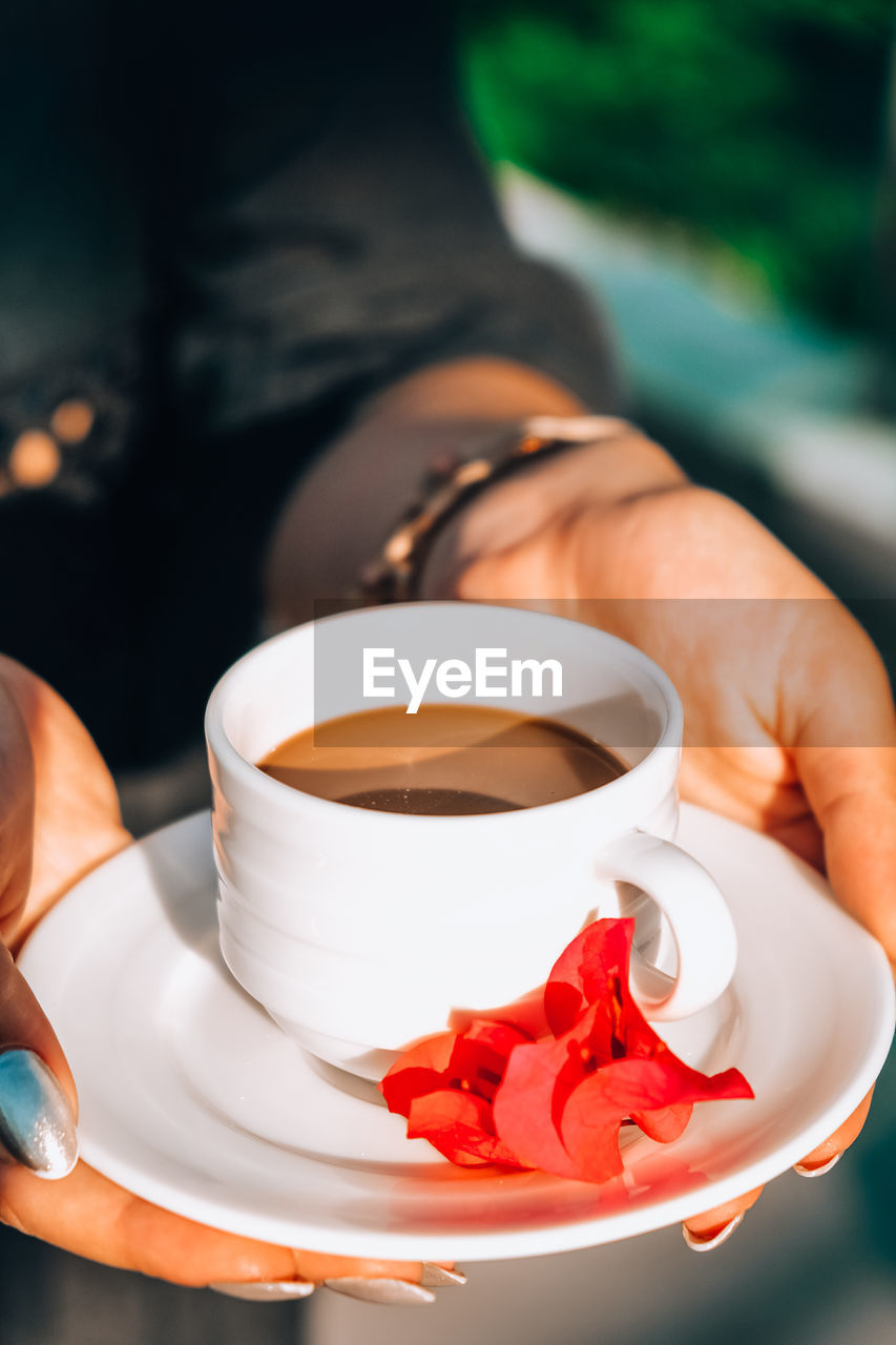 Tanned woman holding porcelain cup of hot coffee and pink tropical flower. mug of hot coffee 