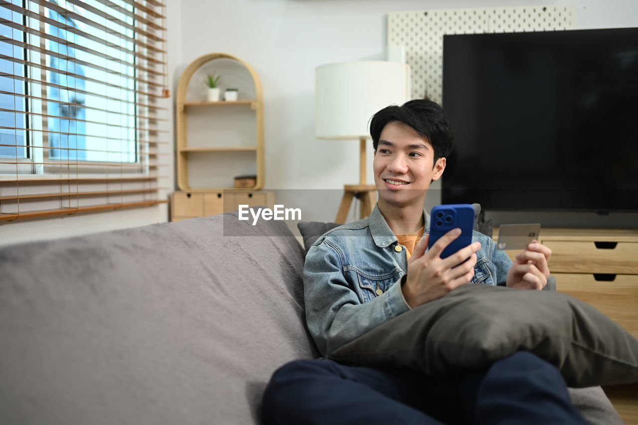 young woman using mobile phone while sitting on sofa at home