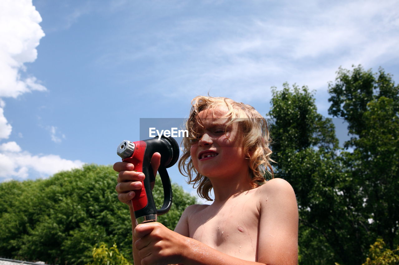 Low angle view of boy holding garden hose