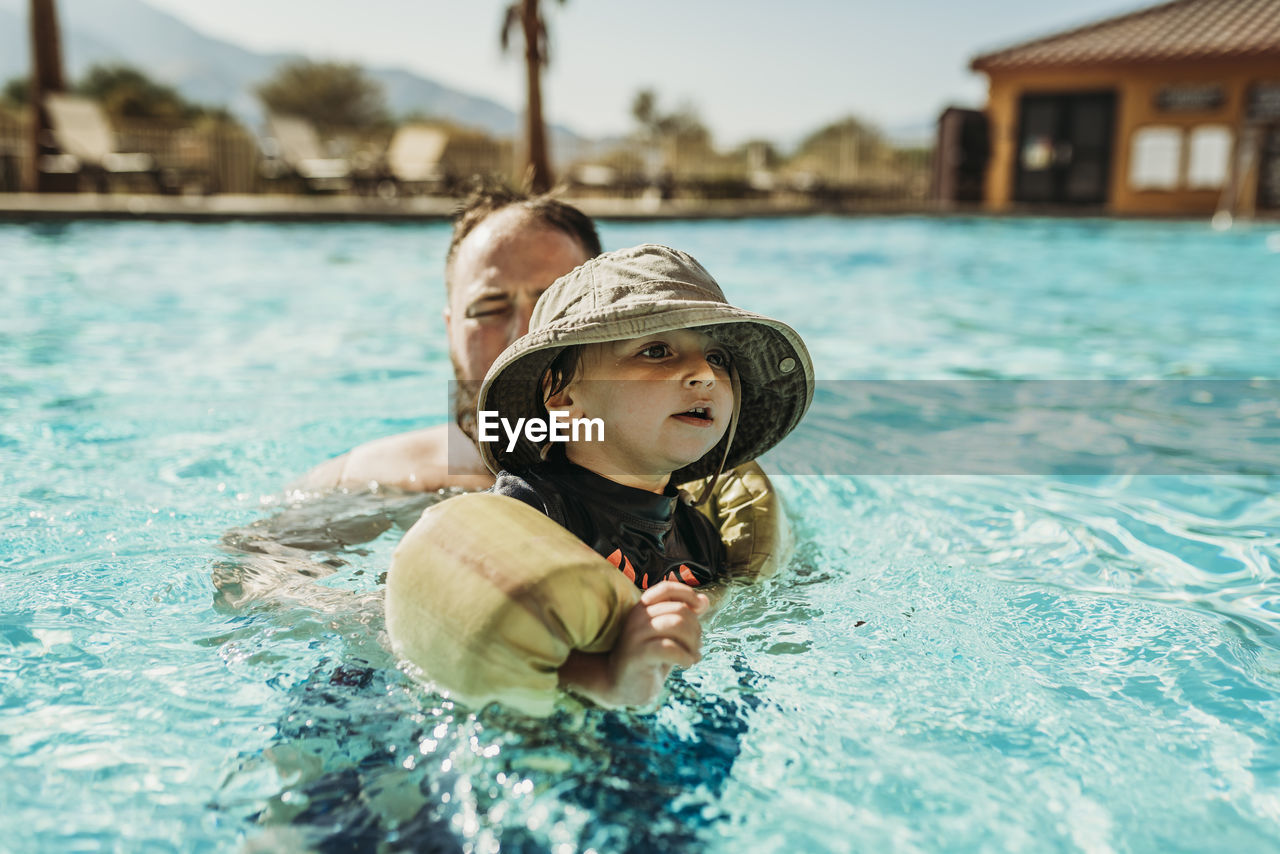 Close up of young toddler boy and father swimming in pool on vacation