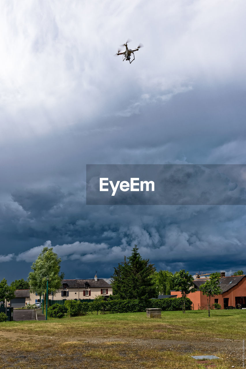 Park and houses against drone flying below cloudy sky