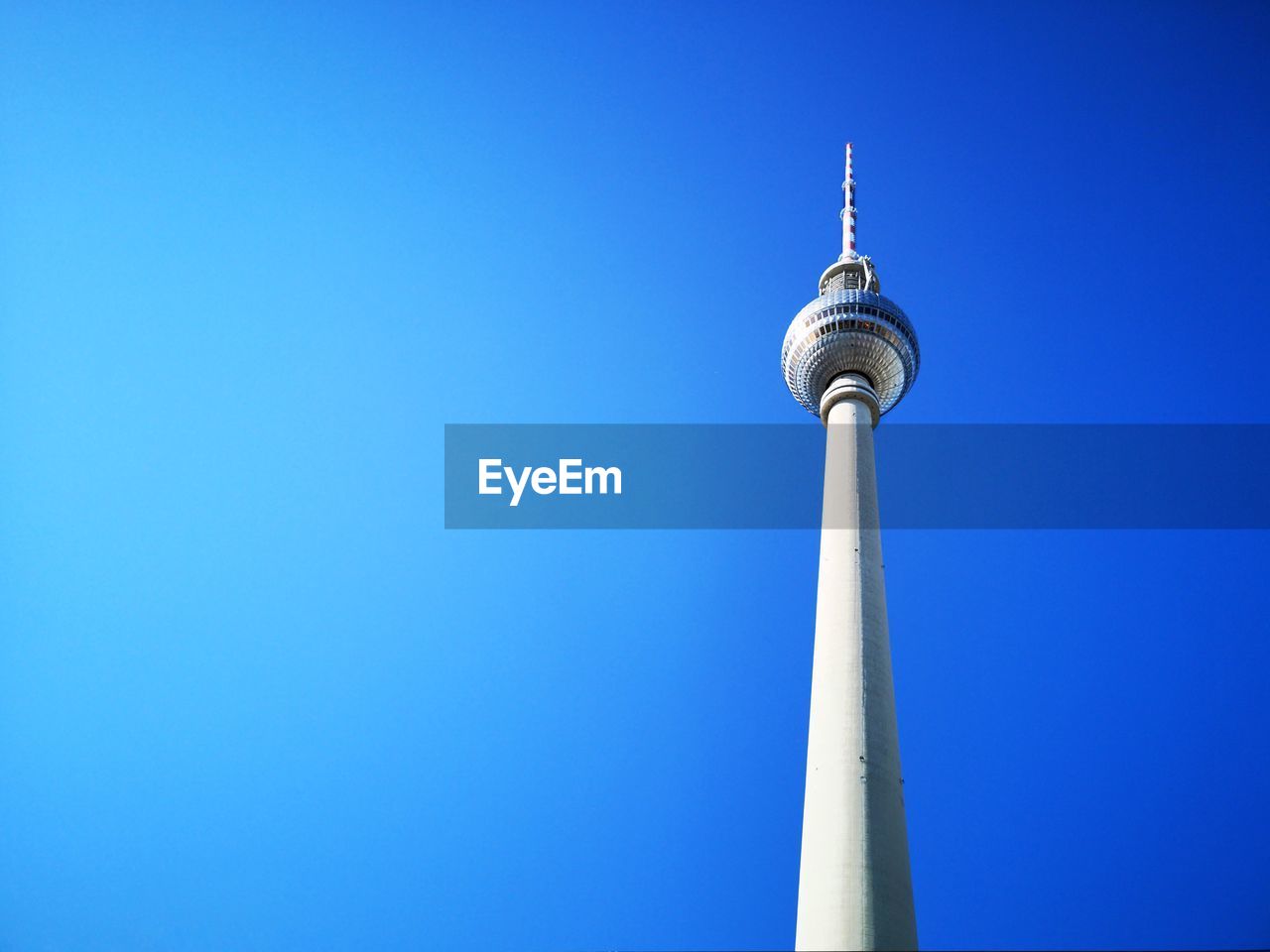 Low angle view of communications tower in city against clear blue sky