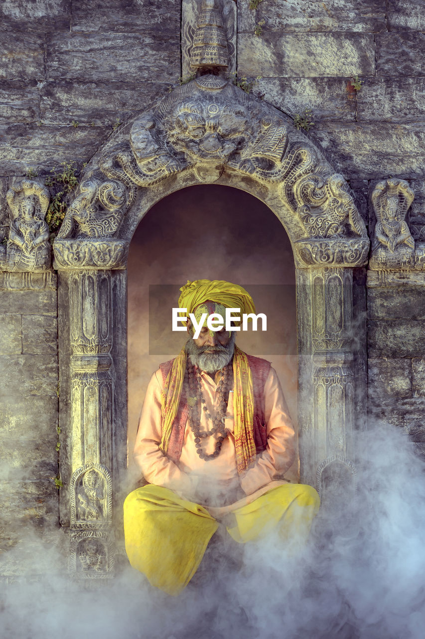 Sadhu sitting amidst smoke against built structure
