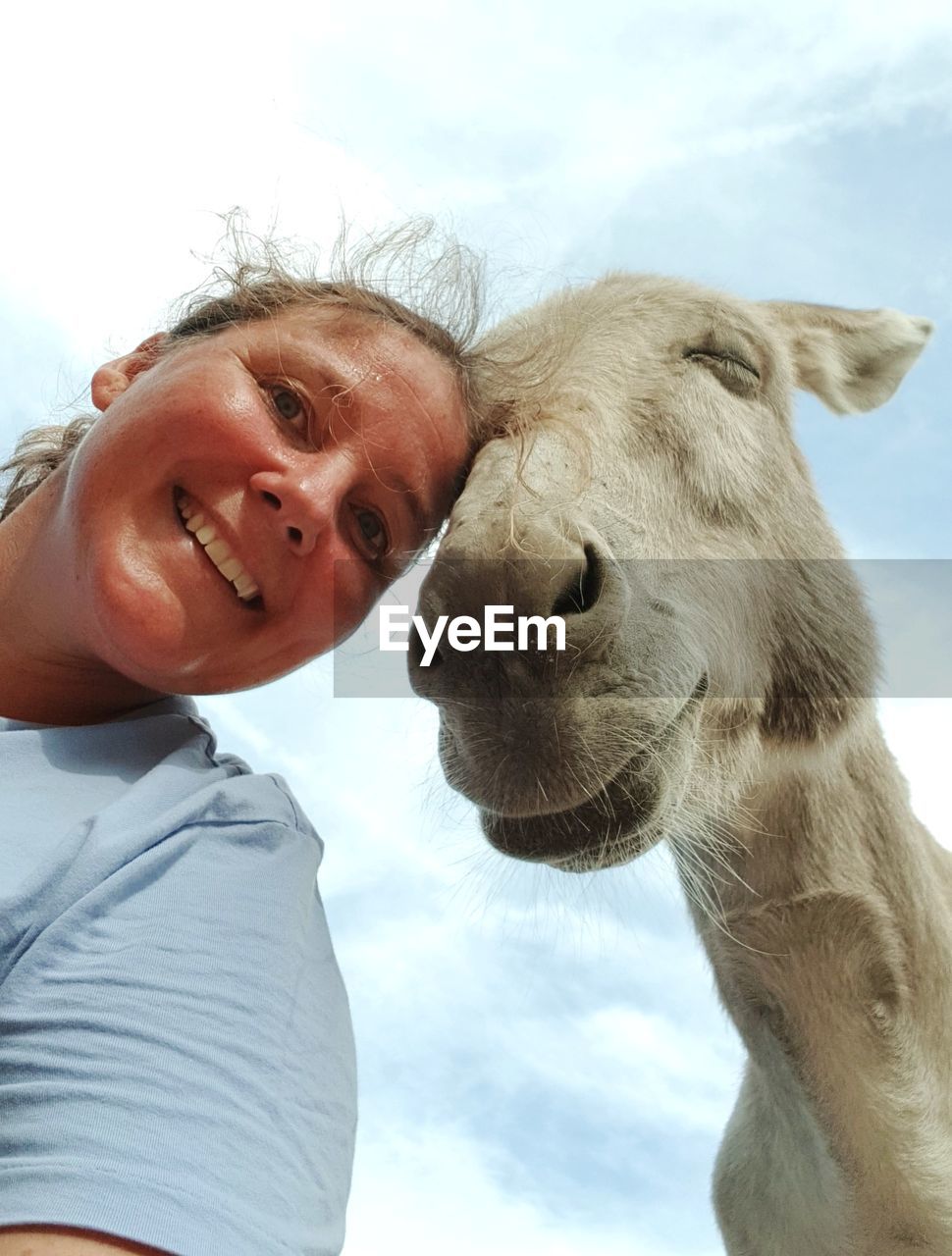 Low angle portrait of woman with horse against sky