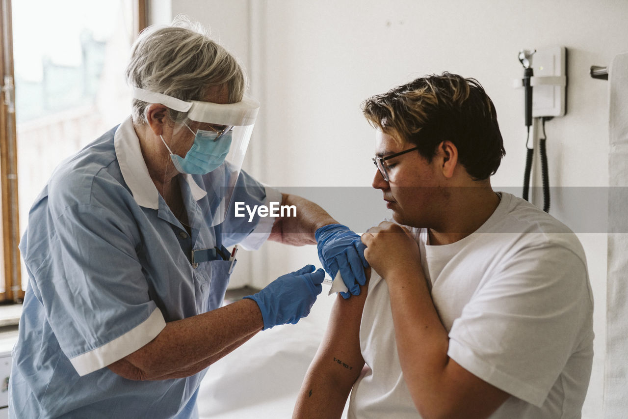 Senior female healthcare worker giving vaccine to young male patient during covid-19