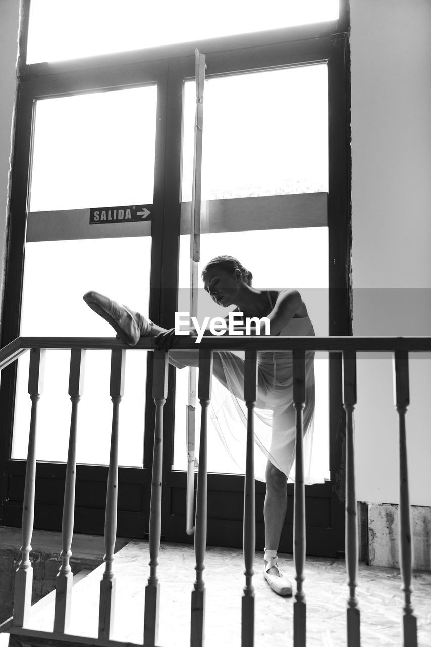 Black and white photo of young woman dancer doing a stretching routine at the entrance of dance studio