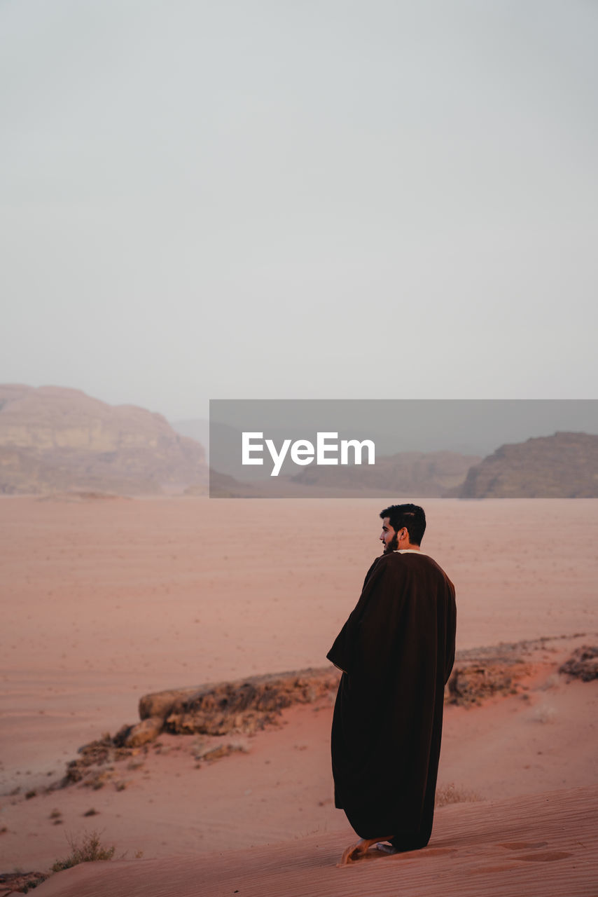 Rear view of man walking at desert against sky