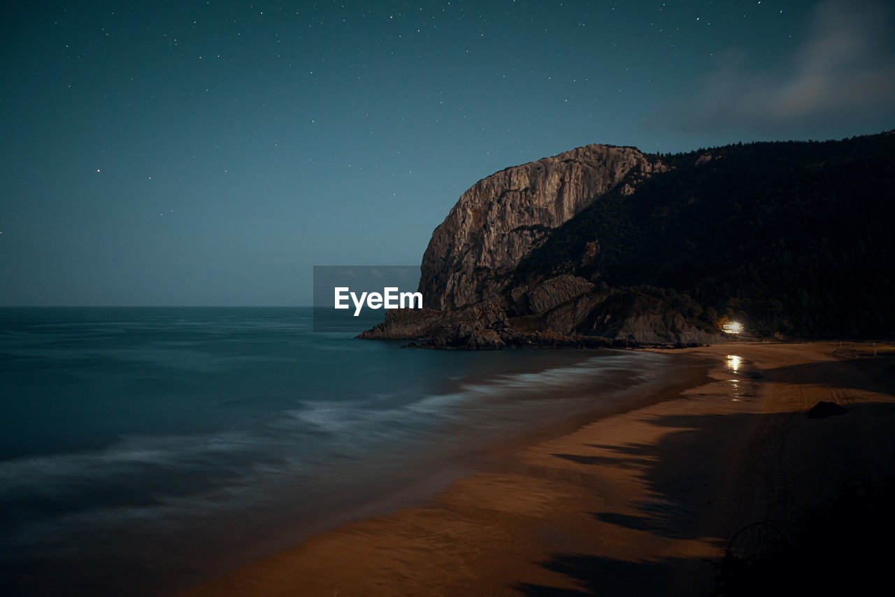 Scenic view of beach and rock against sky at night