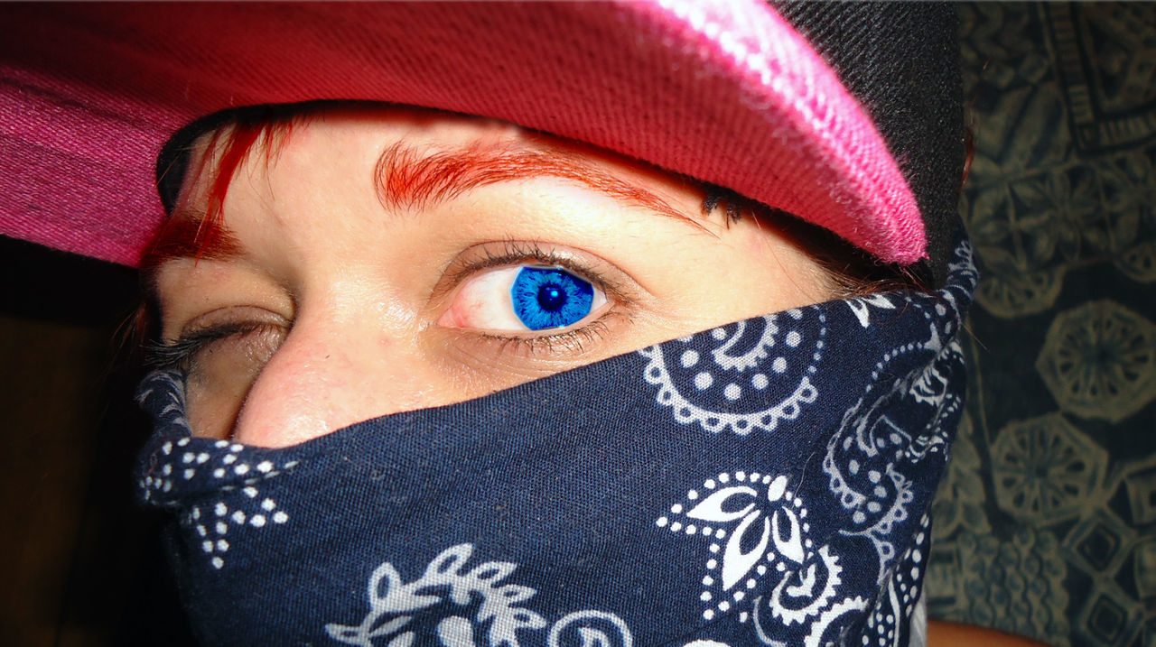 Close-up portrait of person wearing contact lens while winking by wall