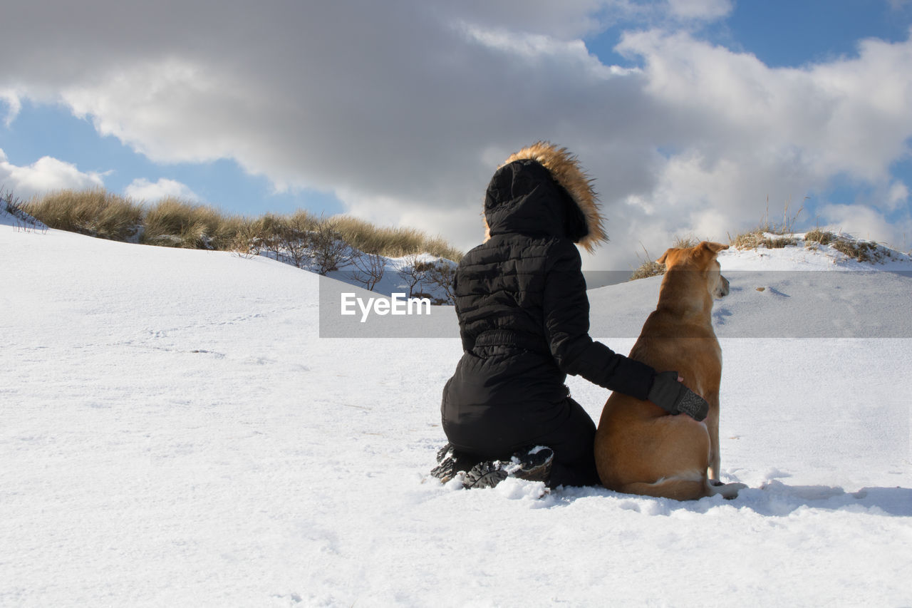 REAR VIEW OF PERSON WITH DOG ON SNOW