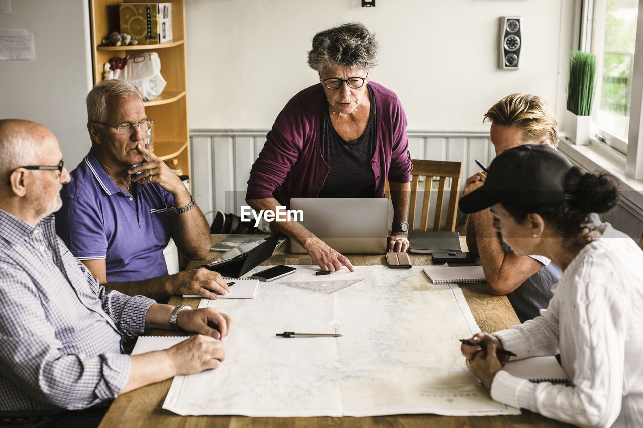 Female instructor explaining senior men and woman over map at table during navigation course