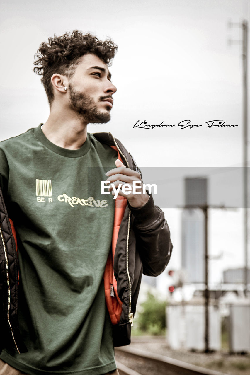 YOUNG MAN LOOKING AWAY WHILE STANDING OUTDOORS