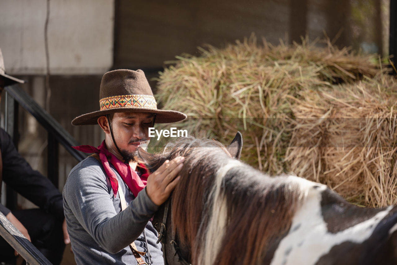 In an outdoor barn, one man dressed as a cowboy trains his horse to run in a circle around him.