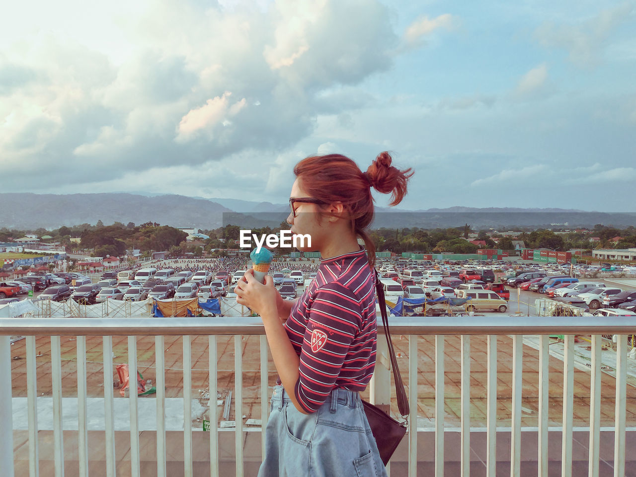 WOMAN STANDING ON RAILING LOOKING AT CITYSCAPE