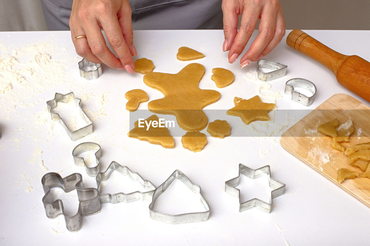 Female hands cut out christmas cookies from dough, using metal molds, on a white table.