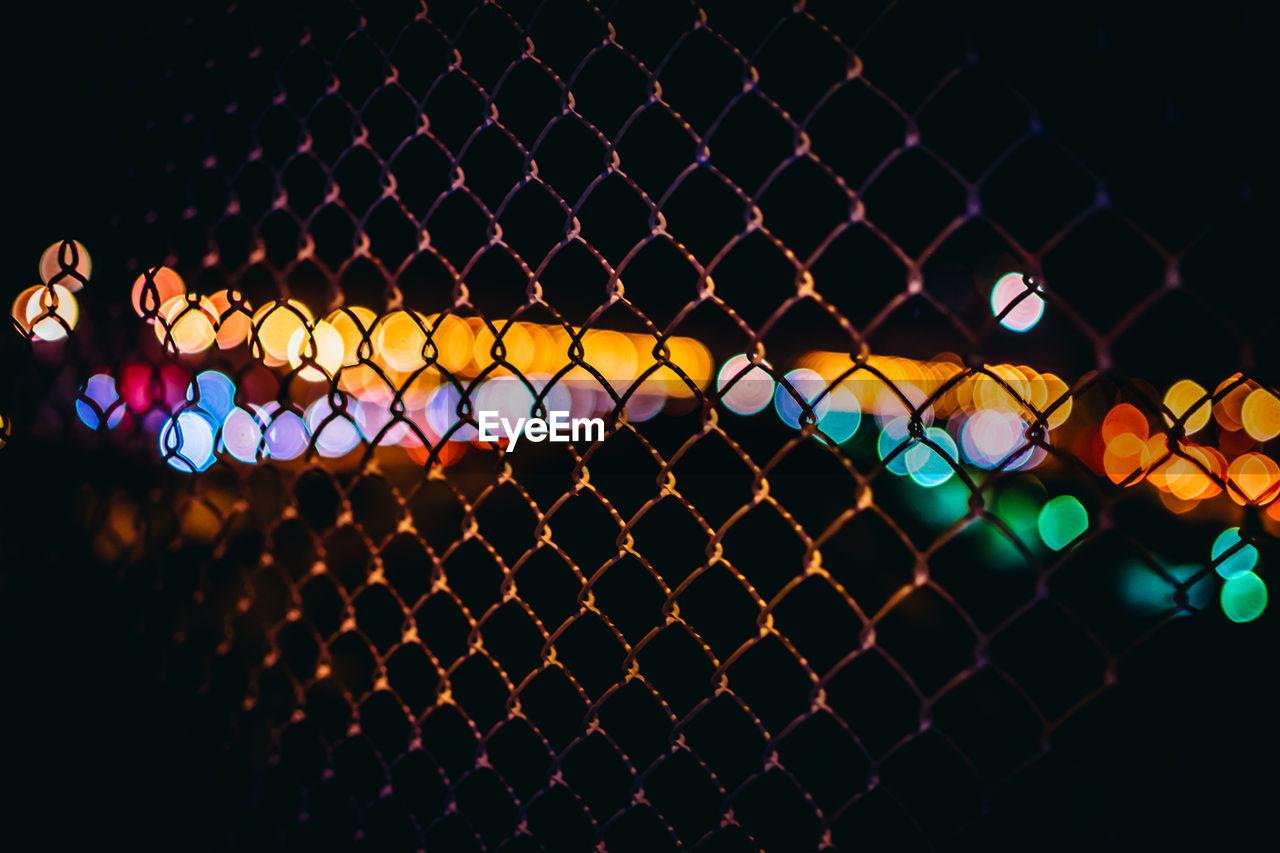 Close-up of chainlink fence against defocused lights at night